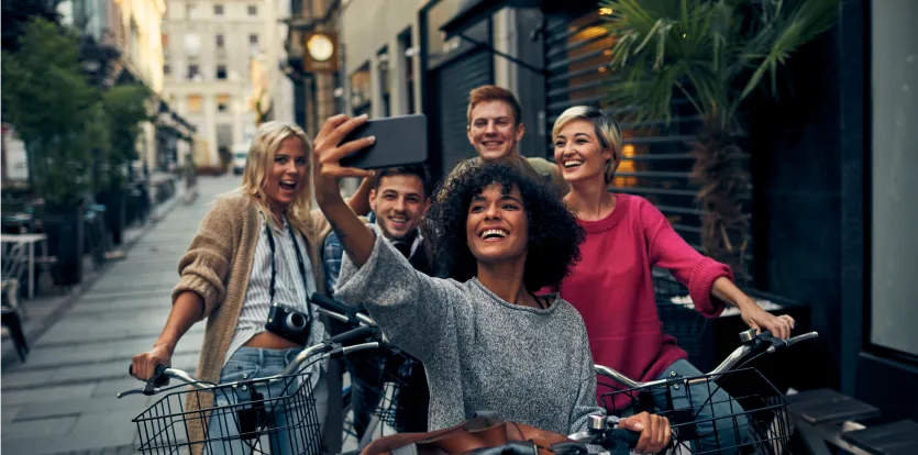 Grupo de amigos jóvenes sonriendo mientras andan en bicicleta y se toman una selfie